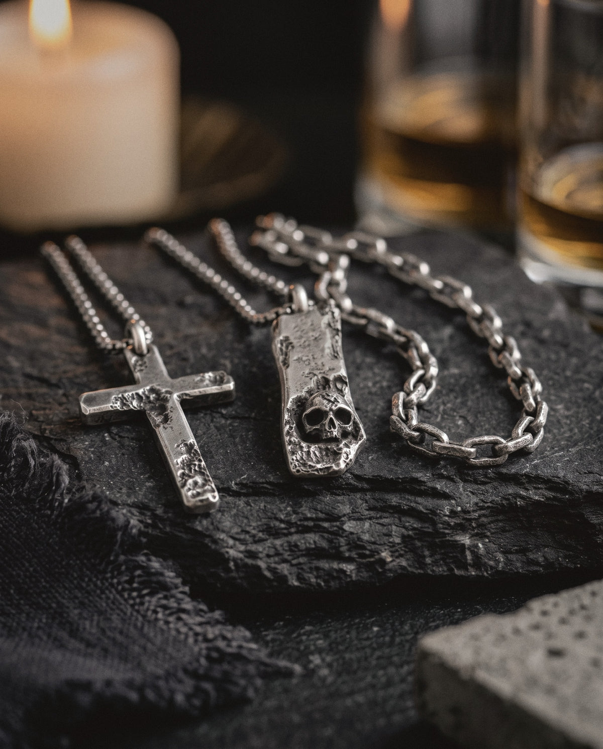Cross pendant, skull bar pendant and cratered link necklace in raw silver on dark slate