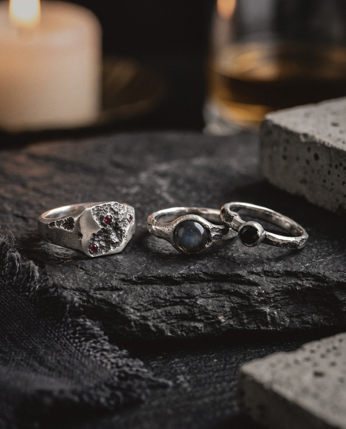 Ruby signet, labradorite ring and black spinel ring in raw silver on dark slate by candlelight