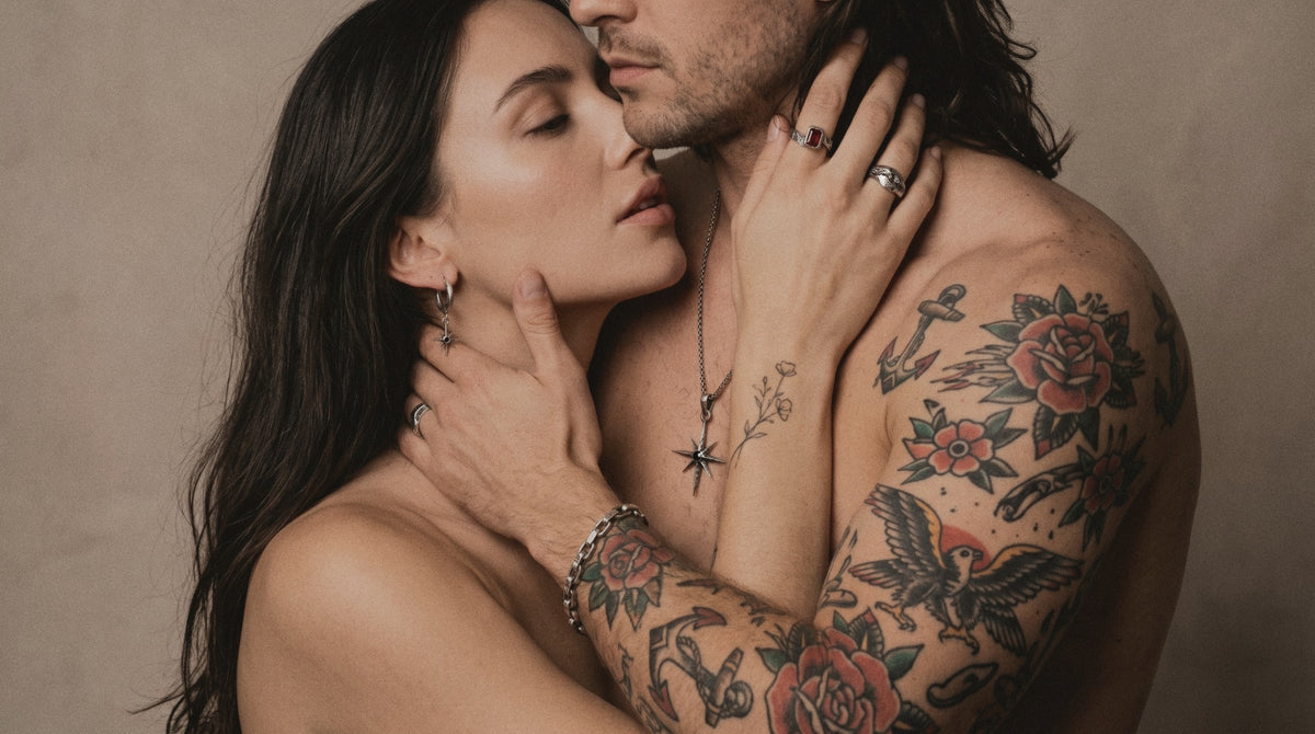 Tattooed couple in an embrace wearing a star pendant, a star hoop earring, a ruby ring, a cratered ring and a link chain bracelet in raw silver